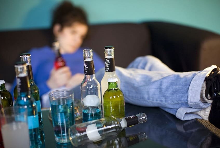парень сидит на диване перед бутылками с алкоголем